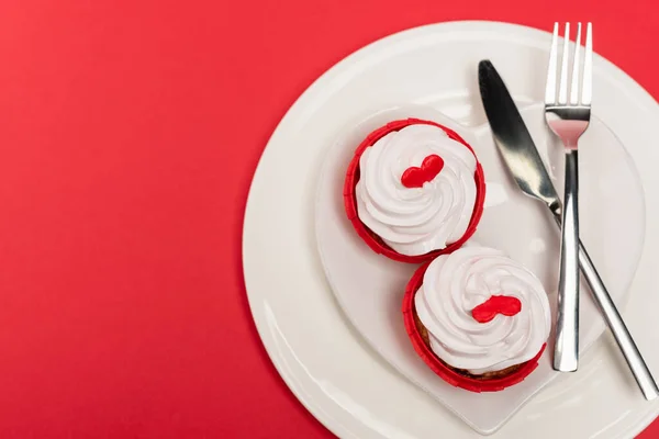 Vista superior de cupcakes en placa con cubiertos sobre fondo rojo - foto de stock