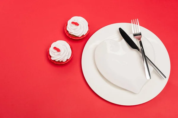 Top view of cupcakes near plate with cutlery on red background — Stock Photo