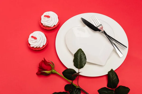 Cupcakes near plate and rose on red background — Stock Photo