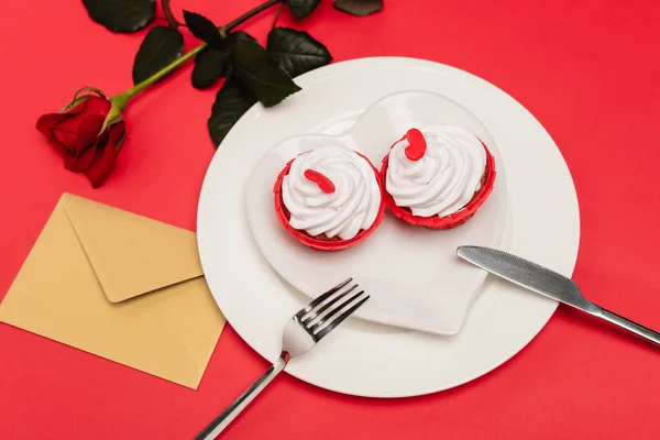 Cupcakes on plate near rose and envelope on red background — Stock Photo
