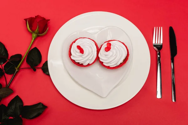 Vue de dessus des cupcakes sur assiette près de rose sur fond rouge — Photo de stock