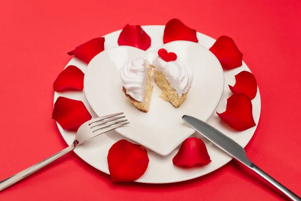 Кекс на тарелке с лепестками роз и столовые приборы на красном фоне — стоковое фото