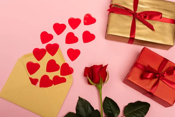 Vista dall'alto di cuori rossi, rosa, busta e scatole regalo su sfondo rosa — Foto stock