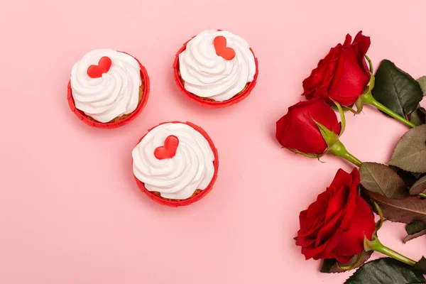 Top view of red roses and cupcakes on pink background — Stock Photo