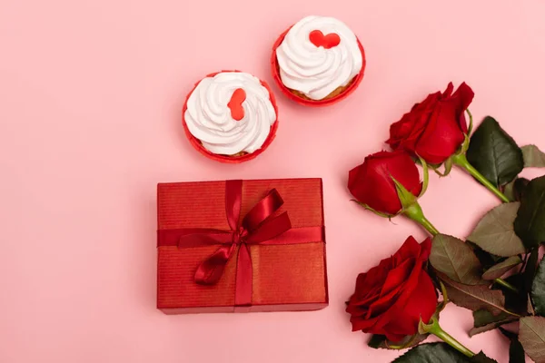 Vista superior do presente, rosas vermelhas e cupcakes no fundo rosa — Fotografia de Stock