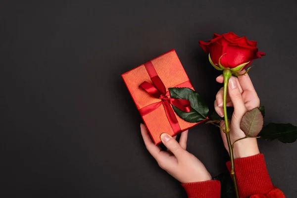 Vista recortada de la mujer sosteniendo rosa roja y regalo aislado en negro - foto de stock