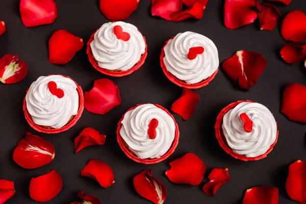 Vista superior de pétalos de rosa y cupcakes de San Valentín aislados en negro - foto de stock