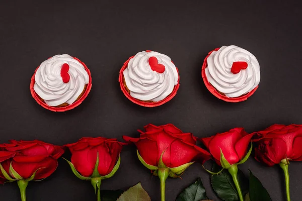 Vista superior de rosas e cupcakes isolados em preto — Fotografia de Stock