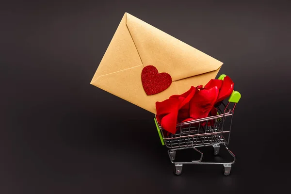 Panier avec pétales de rose et enveloppe isolée sur noir — Photo de stock