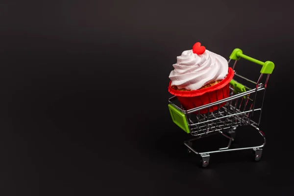 Shopping cart with valentines cupcake isolated on black — Stock Photo