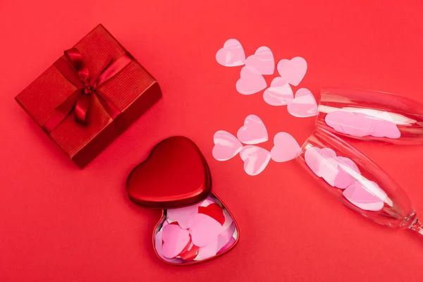 Top view of pink hearts in champagne glasses near gift box on red background — Stock Photo