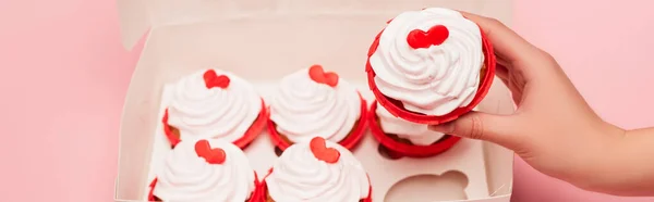 Vista recortada de la mujer sosteniendo cupcake de San Valentín cerca de caja sobre fondo rosa, pancarta - foto de stock