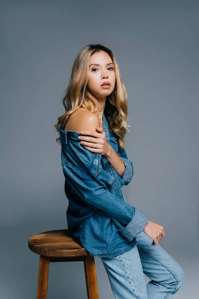 Charming young woman in denim shirt, with naked shoulder, looking at camera isolated on grey — Stock Photo