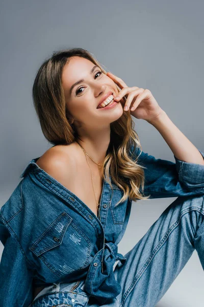 Allegra giovane donna in camicia di jeans in posa con spalla nuda su grigio — Foto stock