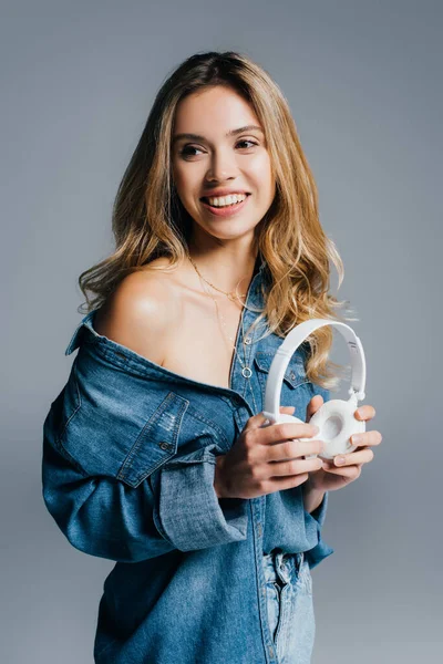 Smiling woman with wireless headphones, wearing denim shirt, with naked shoulder,  isolated on grey — Stock Photo