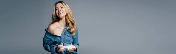 Allegra, donna sexy in camicia di jeans, con spalla nuda, tenendo cuffie wireless isolate sul grigio, banner — Foto stock