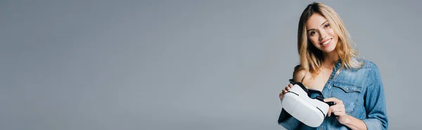 Mulher sorridente em camisa jeans, com ombro nu, segurando vr fone de ouvido isolado em cinza, banner — Fotografia de Stock