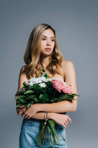 Mujer joven y encantadora con hombros desnudos sosteniendo flores aisladas en gris - foto de stock