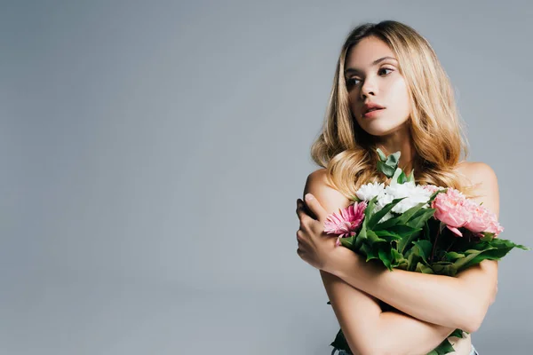 Séduisante jeune femme aux épaules nues tenant bouquet et regardant loin isolé sur gris — Photo de stock