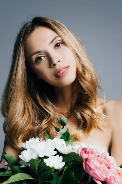 Affascinante giovane donna guardando la fotocamera mentre tiene il bouquet isolato sul grigio — Foto stock