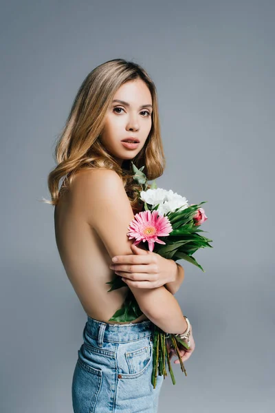 Сексуальна, топлес жінка з квітами дивиться на камеру ізольовано на сірому — стокове фото