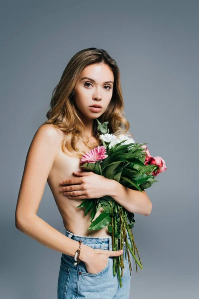 Topless young woman holding hand in pocket of jeans while posing with bouquet isolated on grey — Stock Photo