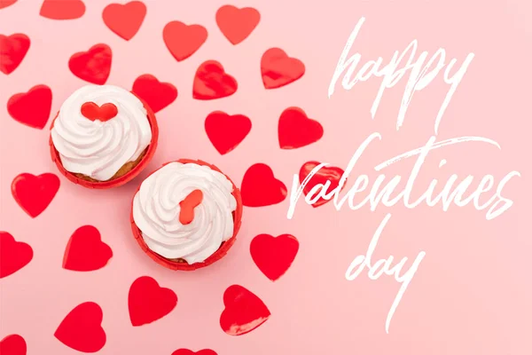 Top view of red hearts and cupcakes near happy valentines day lettering on pink — Stock Photo