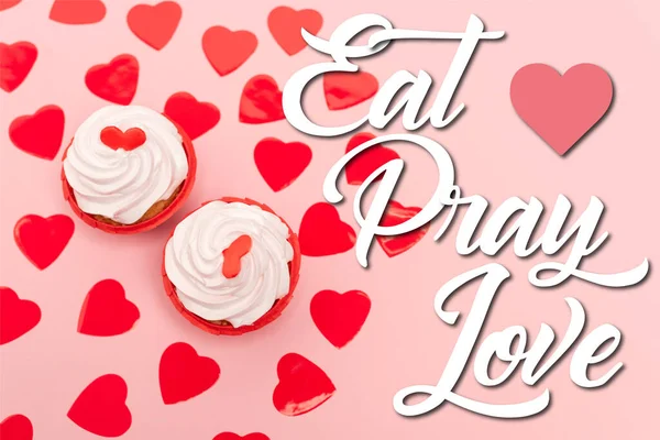 Top view of red hearts and cupcakes near eat pray love lettering on pink — стоковое фото