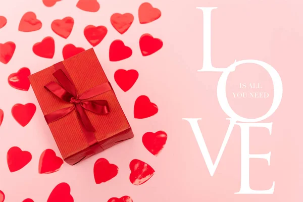 Top view of red hearts and gift box near love is all you need lettering on pink background — Stock Photo