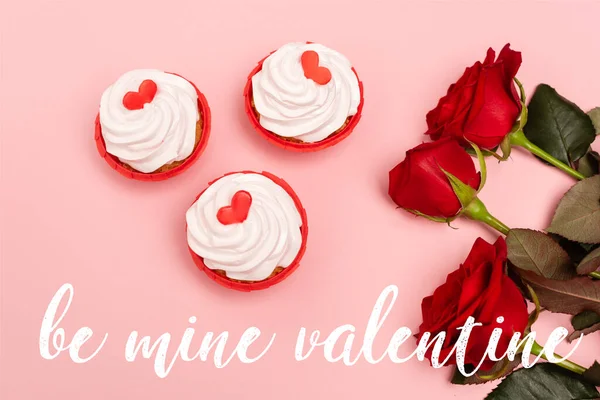 Top view of red roses and cupcakes near be mine valentine lettering on pink — Stock Photo