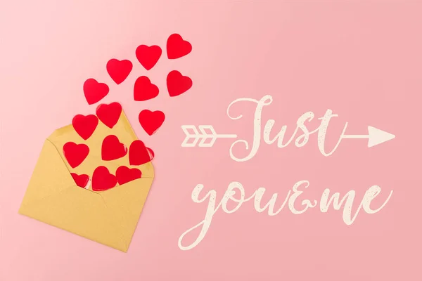 Top view of red paper hearts and envelope near just you and me lettering on pink background — Stock Photo