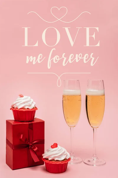 Champagne glasses near gift box, cupcakes and love me forever lettering on pink — Stock Photo