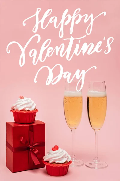 Champagne glasses near gift box, cupcakes and happy valentines day lettering on pink — Stock Photo