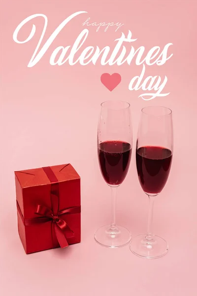 Red wine in glasses near gift and happy valentines day lettering on pink — Stock Photo