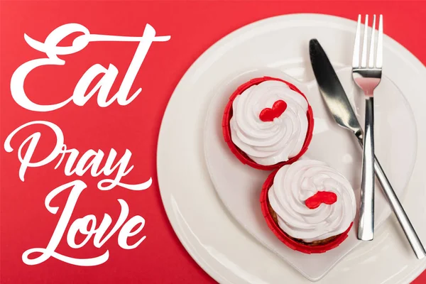 Top view of cupcakes on plate with cutlery near eat pray love lettering on red background — Stock Photo