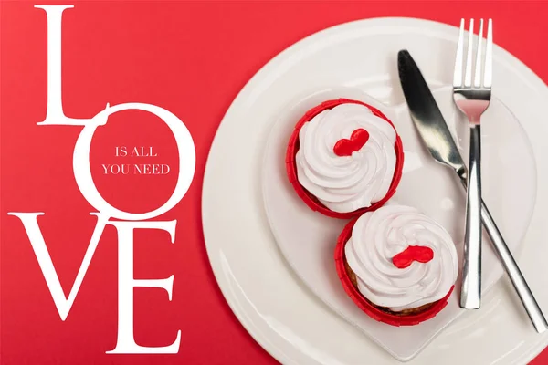 Top view of cupcakes on plate with cutlery near love is all you need lettering on red background — Stock Photo