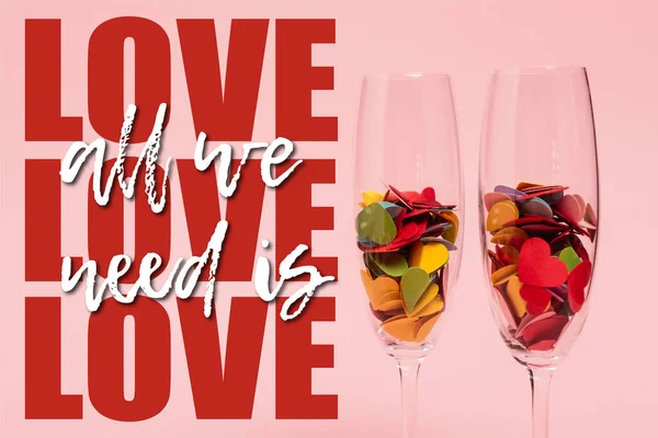 Colorful hearts in champagne glasses near all we need is love lettering on pink — Stock Photo