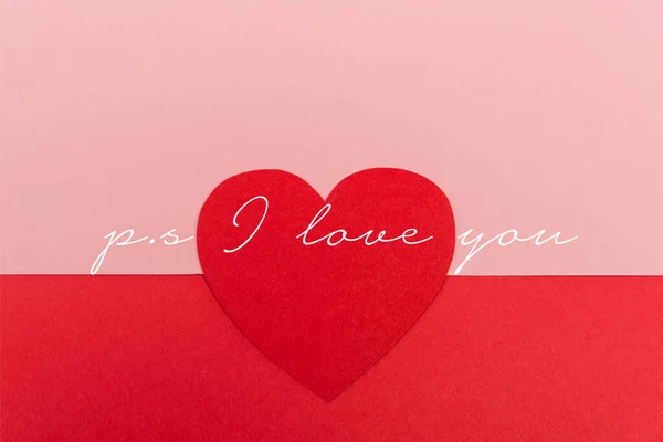 Top view of paper heart near ps i love you lettering on red and pink background — Stock Photo