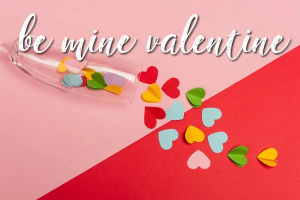 Top view of champagne glass with colorful hearts near be mine valentine lettering on pink and red — Stock Photo