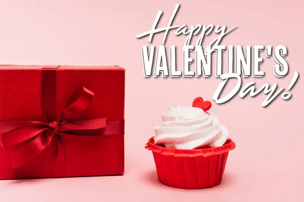 Gustoso cupcake con cuore rosso vicino regalo e felice giorno di San Valentino lettering su sfondo rosa — Foto stock