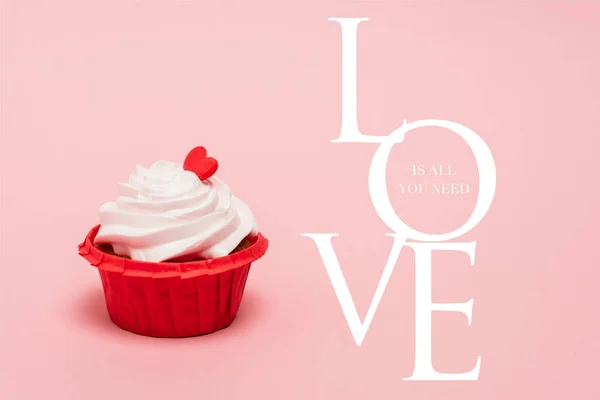 Cupcake de San Valentín con corazón rojo cerca del amor es todo lo que necesita letras sobre fondo rosa - foto de stock