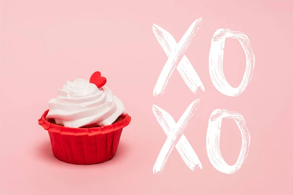 Cupcake de San Valentín con corazón rojo cerca de xoxo letras sobre fondo rosa - foto de stock