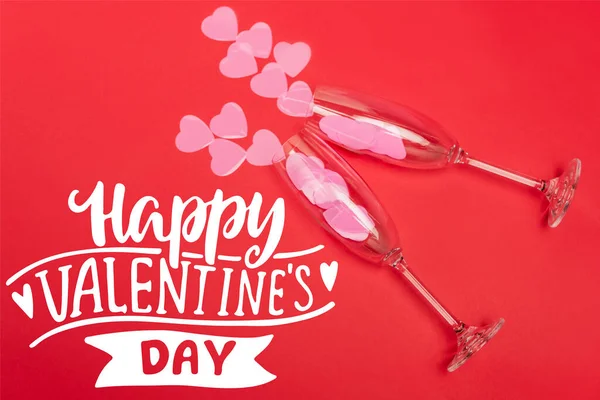 Top view of paper hearts in champagne glasses near happy valentines day lettering on red background — Stock Photo