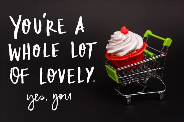 Small shopping cart with valentines cupcake near you re a whole lot of lovely, yes you lettering on black — стоковое фото