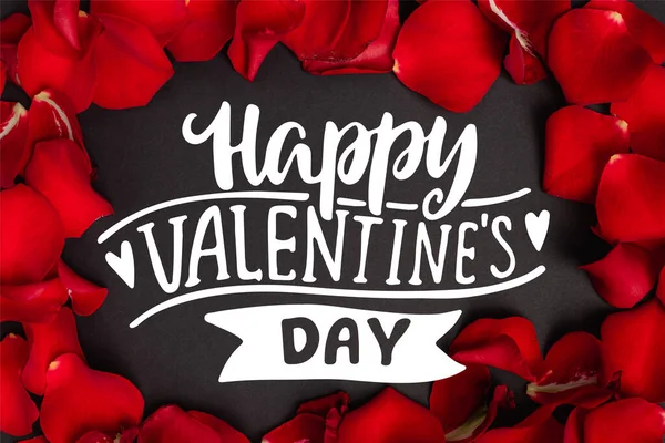 Top view of happy valentines day lettering in frame with red rose petals on black — Stock Photo
