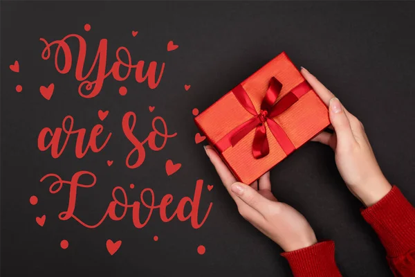 Cropped view of woman holding red gift near you are so loved lettering on black — Stock Photo