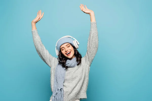 Mulher alegre com as mãos no ar ouvindo música em fones de ouvido isolados em azul — Fotografia de Stock