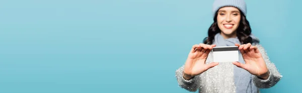 Кредитна картка в руках розмитої щасливої жінки на фоні ізольовано на синьому, банер — стокове фото