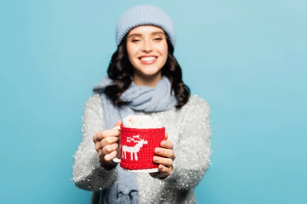 Coupe avec guimauves et porte-tricot dans les mains d'une femme floue sur fond isolé sur bleu — Photo de stock