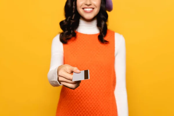 Vista ritagliata di donna bruna riccia dando carta di credito isolata sul giallo su sfondo sfocato — Foto stock